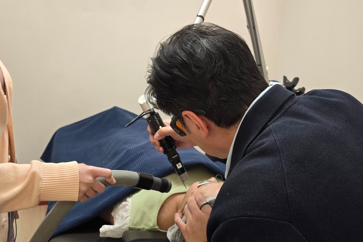 Dr Ong Jin Khang wearing laser safety goggles performing a pigment laser treatment on a patient seated in a clinical chair