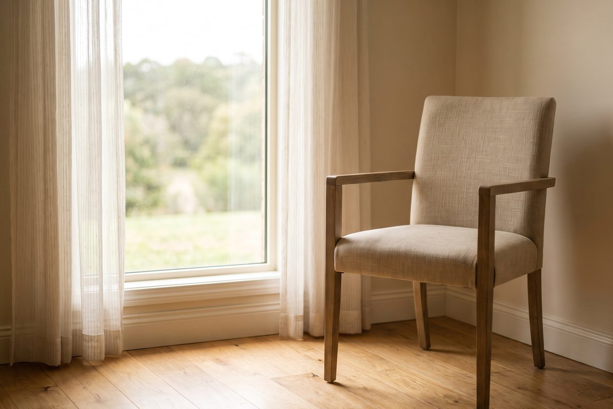 A plain daylight photograph of an empty consulting room chair beside a window, calm and undramatic, no people, no body, no product, no lettering