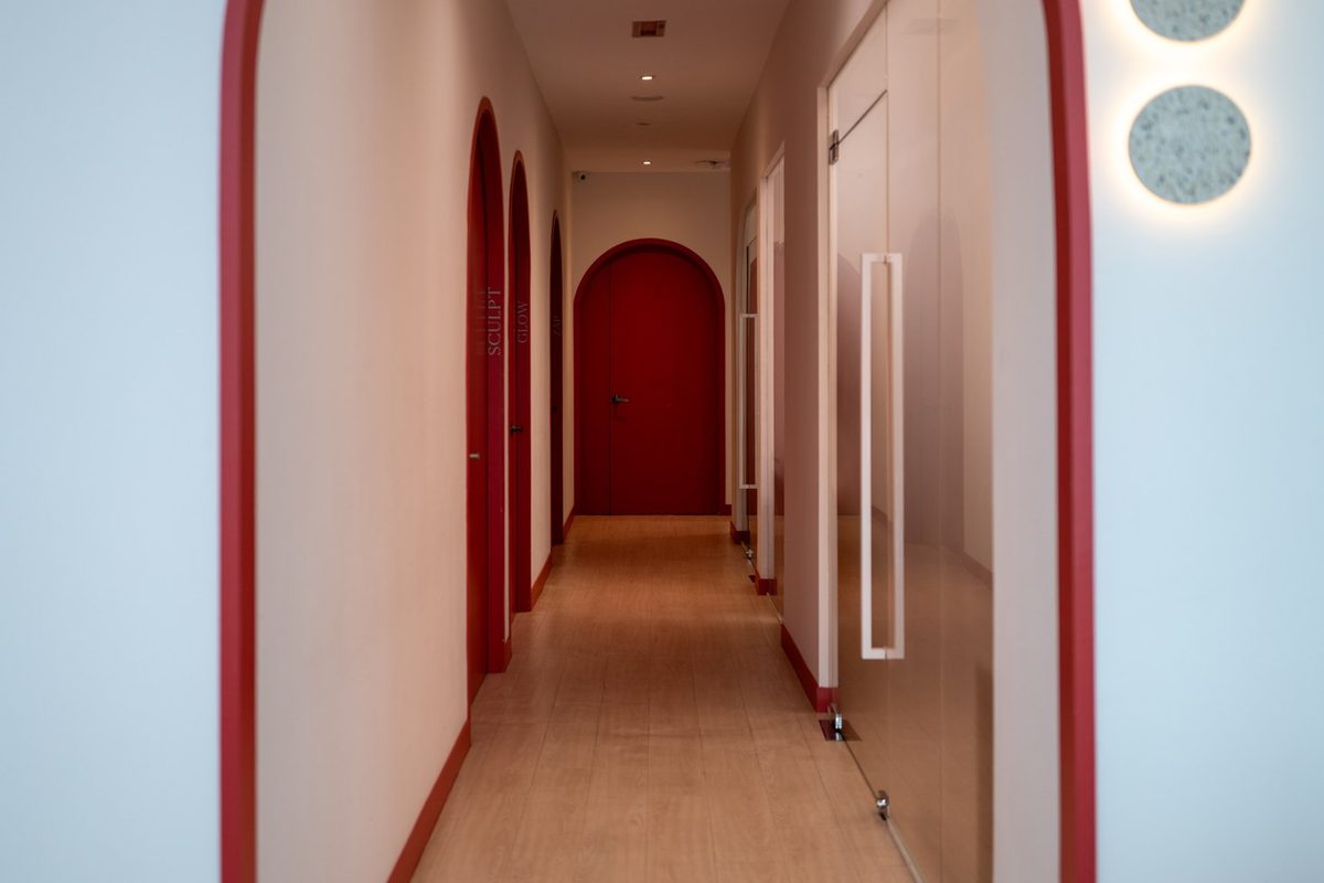 The Retreat Clinic corridor at rest, red arches receding toward a closed red door, nobody in frame
