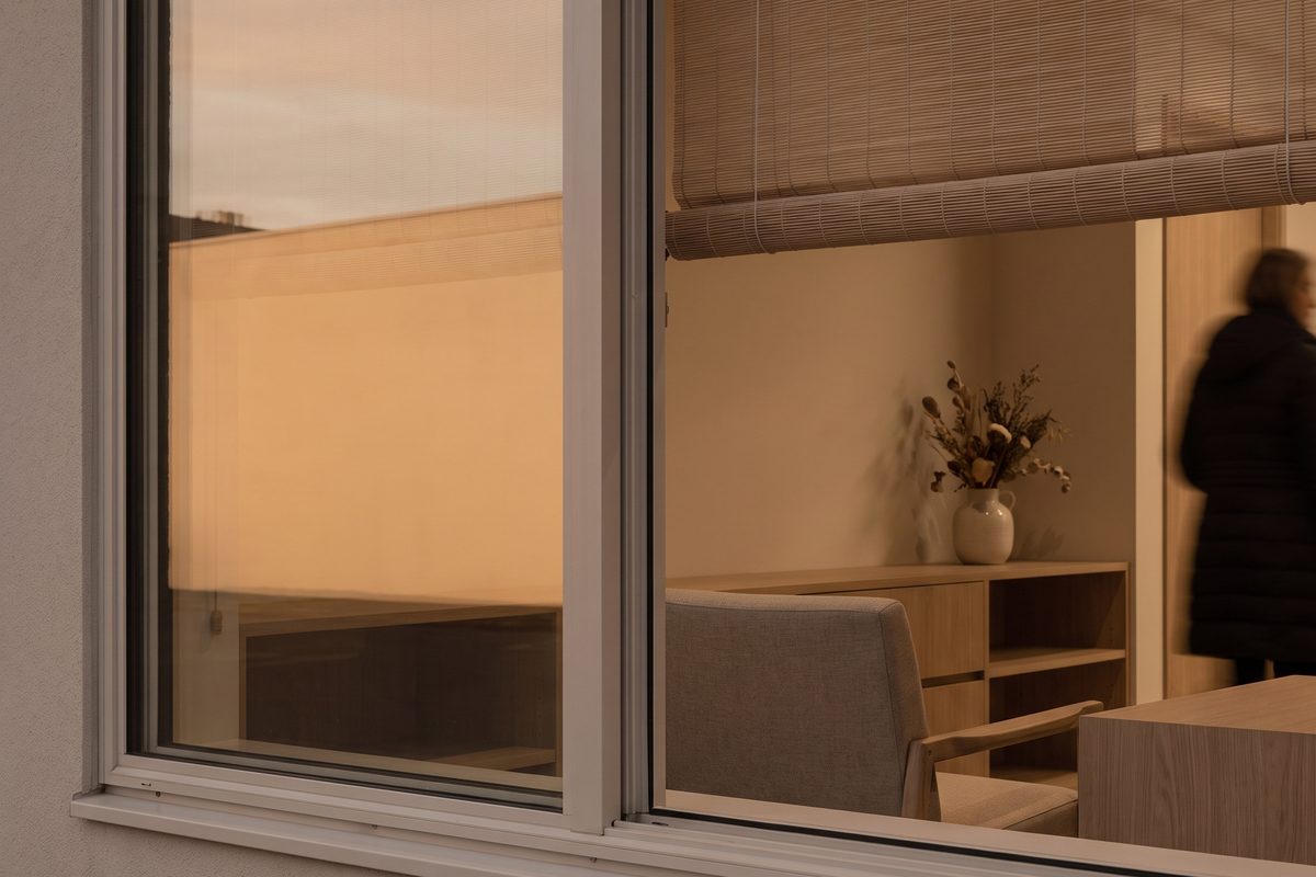 A clinic window in late afternoon, the sky outside softened to a flat amber haze, the room empty and quiet