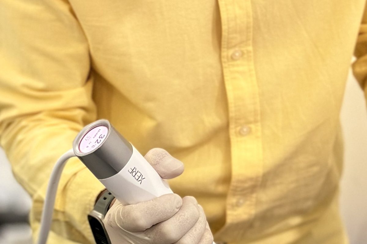 Dr Ong Jin Khang's gloved hand holding the XERF handpiece against gel-sheened skin, the device tip in contact, 32C reading visible on the unit