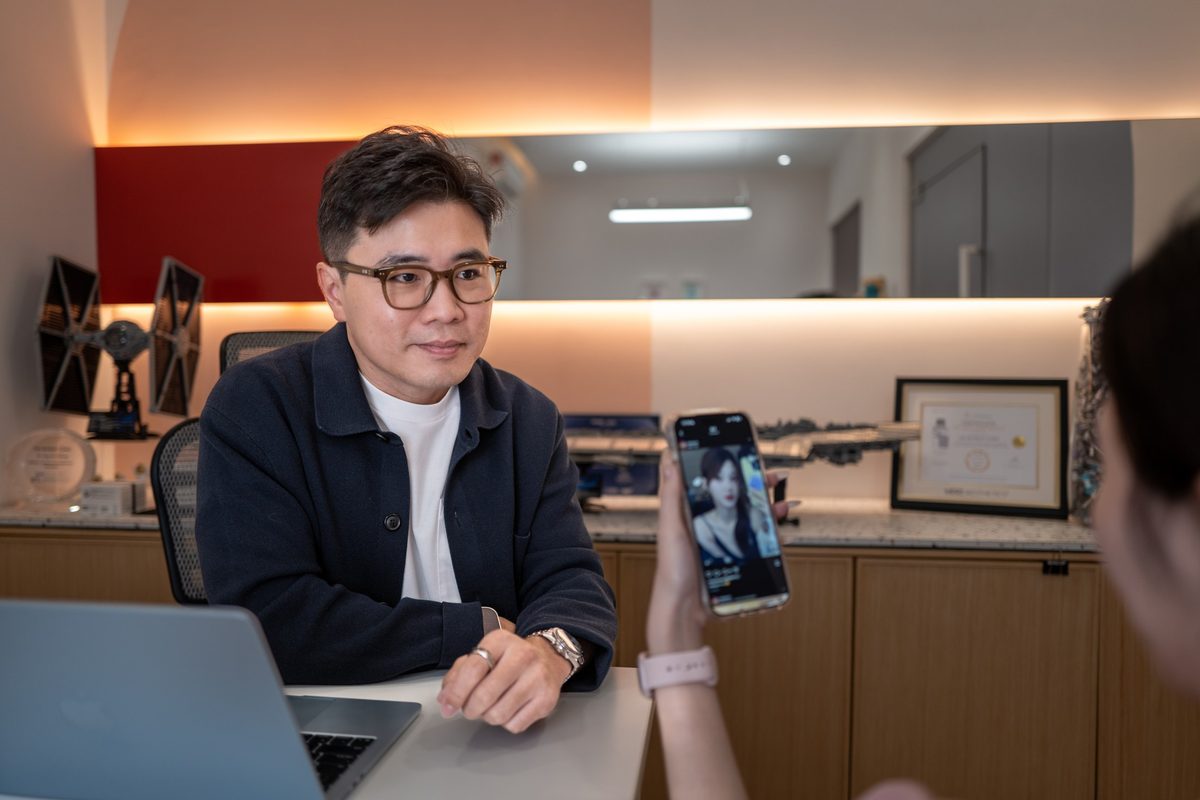 Dr Ong Jin Khang seated at his clinic desk reviewing notes on a laptop, no patient present, warm natural light