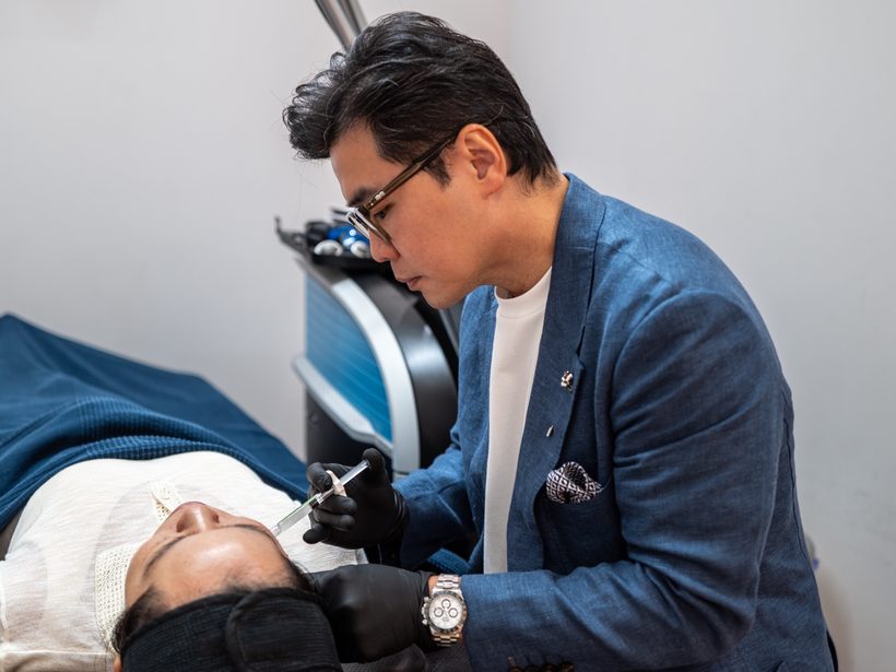 Dr Ong, in a blue jacket and gloves, giving an anti-wrinkle injection to the forehead of a person lying on a treatment couch