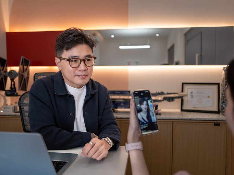 Dr Ong Jin Khang seated at his consultation desk, reviewing notes on a laptop, seen from across the desk in warm clinic light