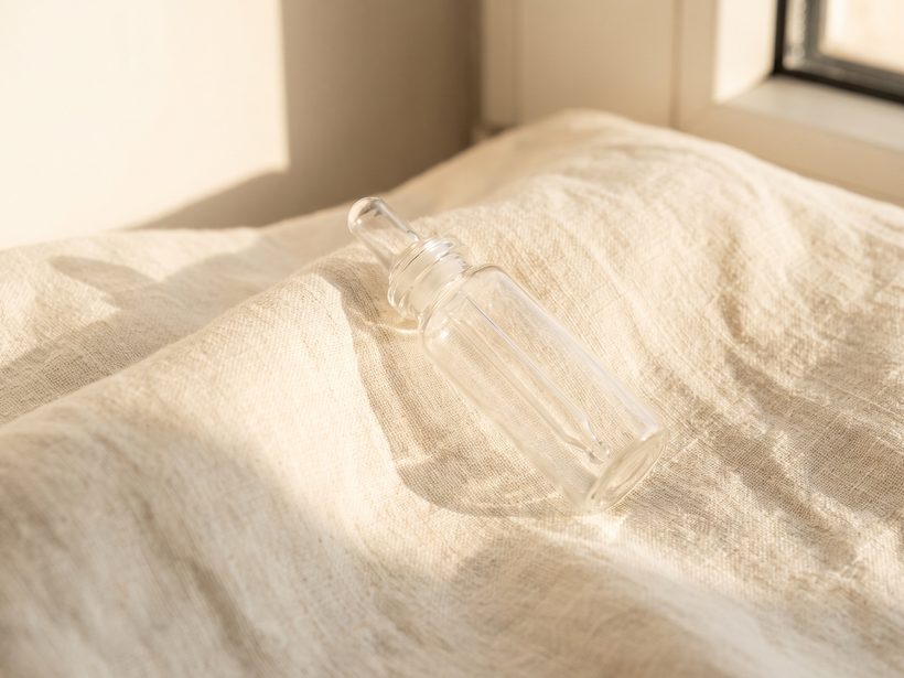 A single glass vial and dropper on plain linen, still life, soft light, no branding and no lettering