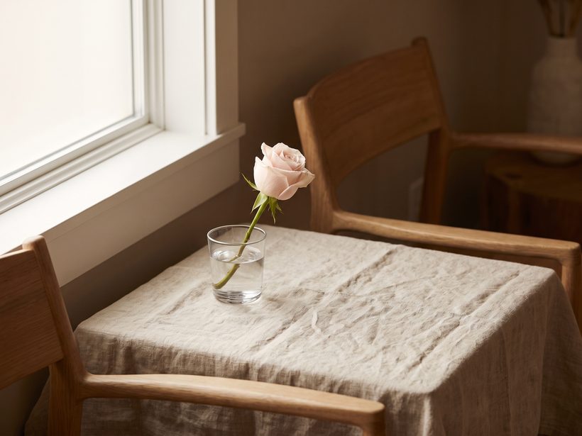 A folded pink silk ribbon on pale linen beside a glass of water in soft daylight, a still life with no people and no medical items in view