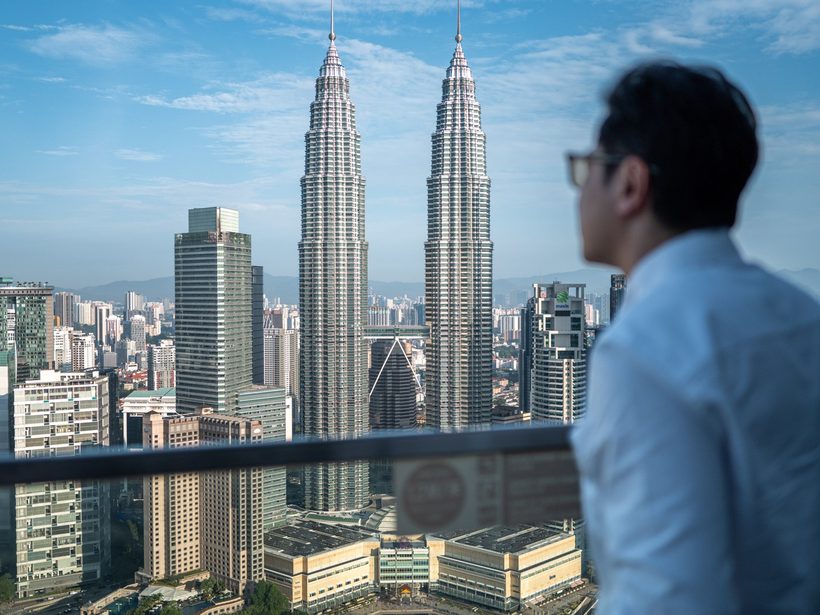 Dr Ong Jin Khang seen from behind in daylight, looking out over a city skyline with two towers standing side by side, no device or treatment in frame