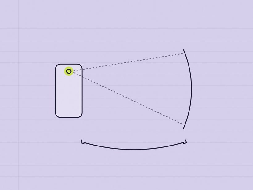 A smartphone standing upright on a desk beside a tape measure, in soft daylight.